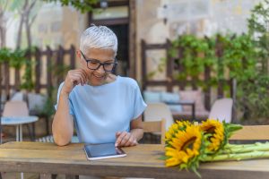 Beautiful senior businesswoman in the cafe, using digital tablet and drinking coffee smiling. Cheerful female entrepreneur is resting after reading electronic book via digital tablet