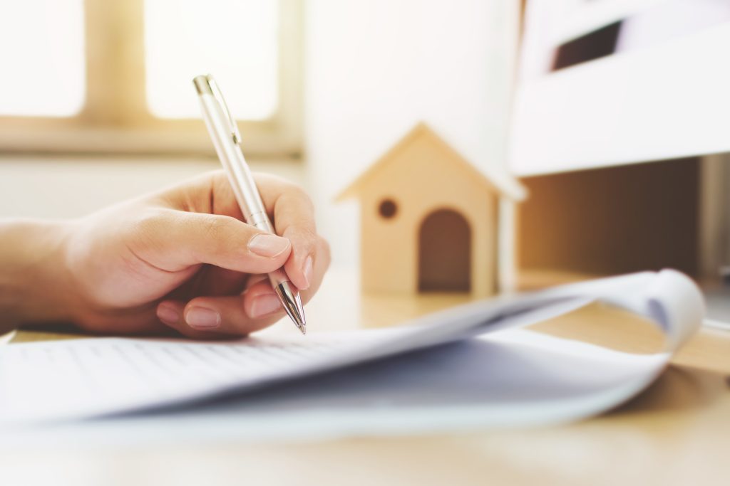 Close up hand of man signing signature loan document to home ownership. Mortgage and real estate property investment